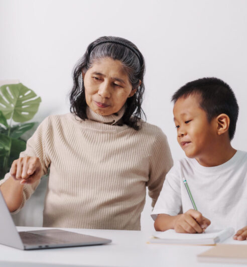 Asian grandson and grandmother people sitting together at desk doing homework at home.