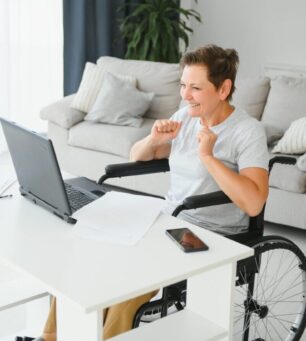 Positive elderly woman in wheelchair working on laptop, IT freelancer, online.